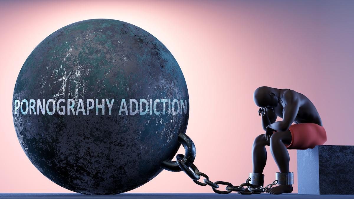 Man chained to a heavy weight with porn addiction writen on it